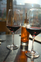 Two wine glasses with red wine and a bottle with chili oil on a table in a restaurant in backlight with reflections