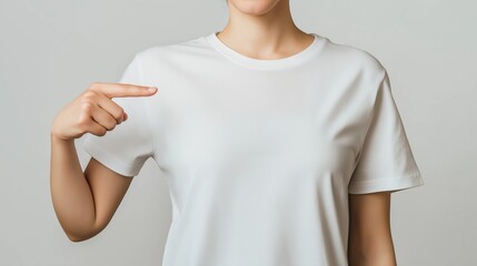 A person in a plain white t-shirt pointing at their chest isolated on light grey background.