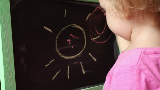 A small child draws with chalk on a blackboard. The child learns to write. Children's education