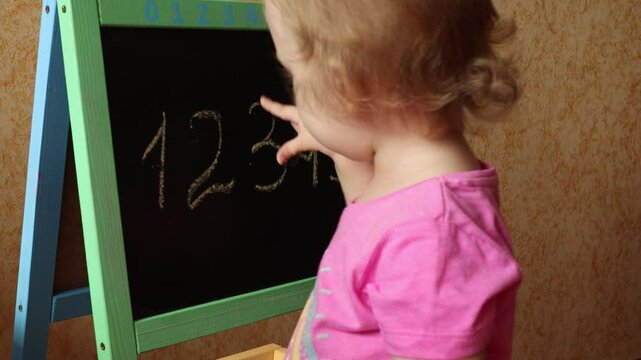 A small child draws with chalk on a blackboard. The child learns to write. Children's education