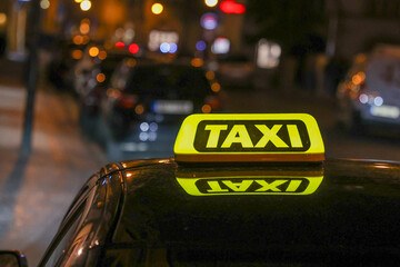 Close-up view of a brightly illuminated yellow taxi sign on the roof of a vehicle. 