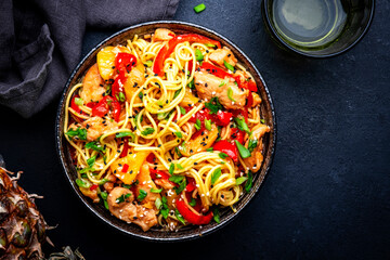 Stir fryed noodles with chicken slices, pineapple, red paprika, onion, soy sauce, garlic, ginger and sesame seedsl. Black background, top view