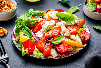Grill salad with red and yellow paprika, feta cheese, walnut, onion, green basil, black background, top view