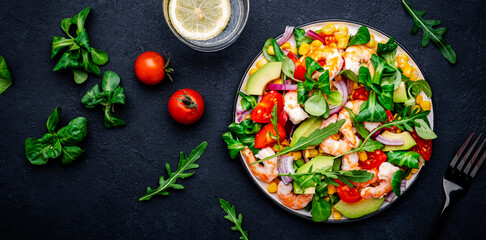 Foodie food salad with shrimps, corn, avocado, tomatoes, lamb lettuce, arugula and red onion on black background. Top  view