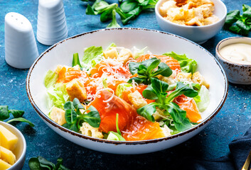 Foodie food caesar salad with salmon, iceberg  lettuce, croutons, grated parmesan with dressing. Blue background, top view