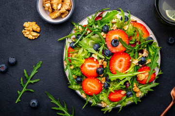 Vegan strawberry and herbs salad with arugula, blueberries and walnuts on black background. Top view