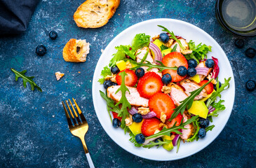 Foodie food salad with strawberry, chicken, arugula, blueberries, avocado and walnuts, blue table., top view