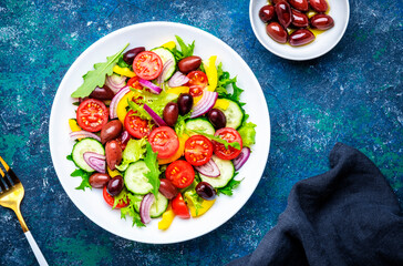 Vegan salad with olives, tomatoes, paprika, cucumber, lettuce and onion. Blue background, top view