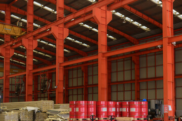 200-liter red steel drums are lined up in a warehouse equipped with an electrically controlled heavy-duty crane inside an industrial plant.