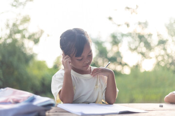 A young girl is sitting at a table with a pencil and a piece of paper