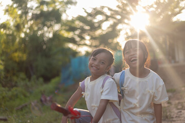 Two young children are smiling and standing next to each other in a park.