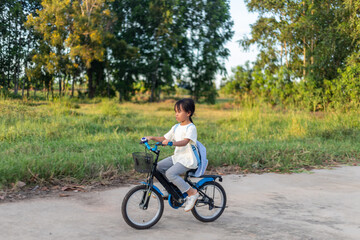 Fototapeta premium A young girl is riding a bicycle with a basket on the front. She is wearing a white shirt and grey pants.