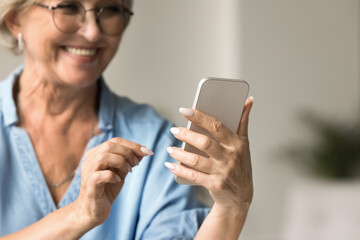 Close up happy older woman using her smartphone, typing message, choose goods, buying services, enjoy remote chat with friend or online communication, read news, check planner or organizer using app