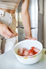Unrecognizable woman pouring smoked paprika to chicken with spices in a kitchen