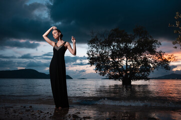 Beauty and nature. Fairy and sensual portrait of pretty young woman wearing long black dress against dramatic sky and sea view