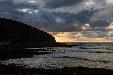 Obraz premium Dramatic sunset over rocky shore of Pacific Ocean near Raglan, New Zealand