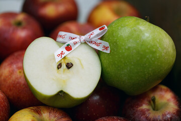 Freshly cut apple beside a whole green apple amidst of red apples. A ribbon with the Hebrew inscription words shana tova is attached to it which means Happy New Year. Jewish holiday Rosh Hashanah