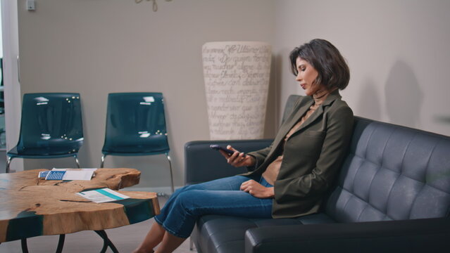 Elegant lady looking cellphone in designed office space. Relaxed businesswoman