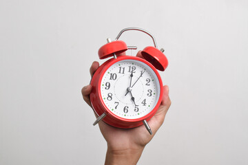 Vintage red alarm clock in hand. Round red alarm clock isolated on white background shows 5 am