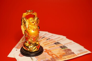 Russian rubles and a smiling Buddha figurine on a red background. Finance and economics.