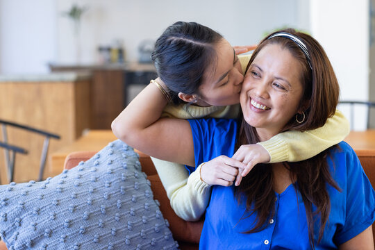 Embracing and kissing asian mother, daughter showing affection and love at home