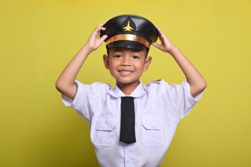 Little Asian boy Beaming airplane pilot holding hat in arms isolated on yellow background. Little boy dreams of becoming an airplane pilot.