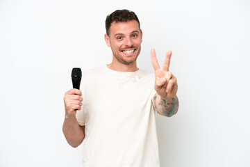 Young caucasian singer man picking up a microphone isolated on white background smiling and showing...