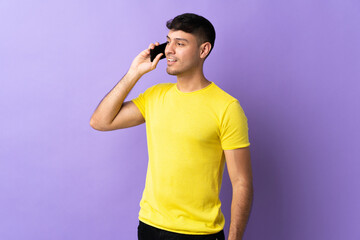 Young Colombian man isolated on purple background keeping a conversation with the mobile phone