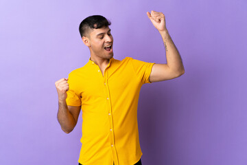 Young Colombian man isolated on purple background celebrating a victory