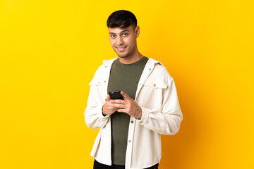 Young Colombian man isolated on yellow background sending a message with the mobile