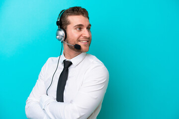 Telemarketer caucasian man working with a headset isolated on blue background with arms crossed and happy