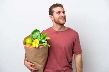 Young caucasian man holding a grocery shopping bag isolated on white background thinking an idea while looking up