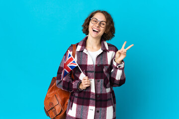 Young English woman holding an United Kingdom flag isolated on blue background smiling and showing victory sign