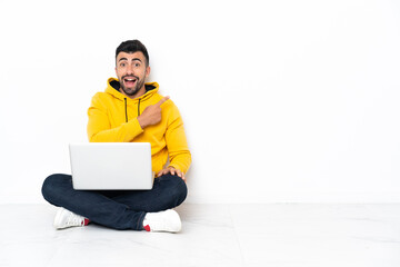 Caucasian man sitting on the floor with his laptop surprised and pointing side