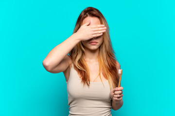 Fototapeta premium Teenager girl brushing teeth over isolated blue background covering eyes by hands. Do not want to see something