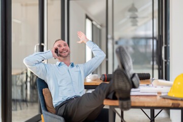 Happy Young Businessman Relaxing and Talking on the Phone in a Modern Office Setting