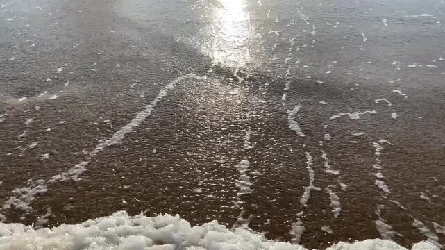 Wellen rollen an den Strand und brechen am Ufer. Das Meer zeigt leichte bis mittlere Bewegungen, w&auml;hrend der Sand am Strand nass und glatt erscheint.