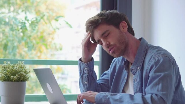 Stressed tired man in pain having strong terrible headache attack after computer laptop work, fatigued exhausted guy suffering from chronic migraine massaging temples to relieve head ache tension
