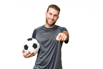Young handsome blonde man over isolated chroma key background with soccer ball and pointing to the front