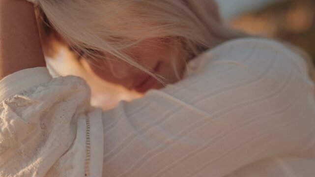 Close up of young attractive blonde woman with a pearl bracelet posing in a white shirt at sunset on a warm summer evening.