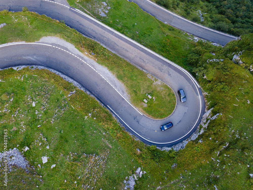 Wall mural two blue cars in harpin curve on mountain road in the swiss alps from above, aerial drone shot, klau