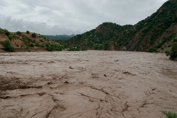 Rushing river full of mud and debris flowing through a valley, a result of heavy rainfall in a...