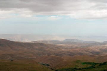 Wide shot of a vast landscape showing rolling hills and valleys stretching to the horizon, creating a sense of endlessness and tranquility. The cloudy sky adds to the serene ambiance