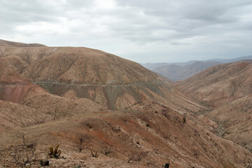Cars driving on a winding mountain road through a barren desert landscape under overcast skies, capturing adventure and exploration in the arid wilderness of a canyon