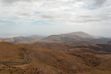 Long and winding road is traversing a vast mountainous landscape, leading towards a distant mountain range. The scene exudes a sense of adventure and the beauty of untouched nature