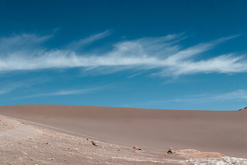 Endless sand dunes stretch across the arid desert under a vibrant blue sky with wispy clouds,...
