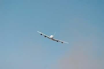 Large passenger plane is flying high in the sky, leaving a trail of white smoke behind it. The plane is tilted slightly, giving a sense of movement and altitude
