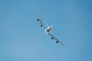 Passenger airplane soars high in the sky, displaying its belly and engines, embodying aviation and travel with speed and power against a sunny backdrop