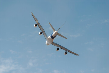 Large passenger jet is banking against a beautiful blue sky with a few white clouds. The airplane has four engines and its landing gear is retracted