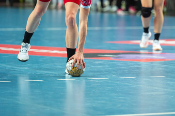 Handball woman player raises ball from parquet during the match.